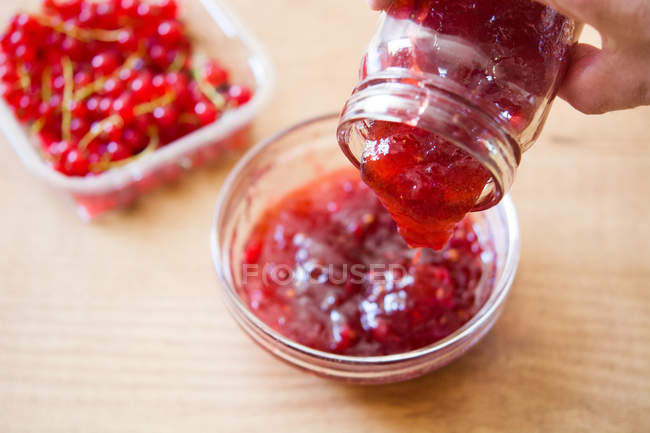 Portion süße rote Beerenmarmelade aus dem Glas in eine Schüssel auf dem Holztisch — Stockfoto