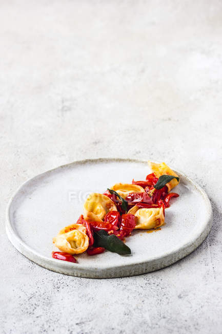 Вкусное блюдо тортеллини с помидорами подается на тарелке на сером столе — стоковое фото