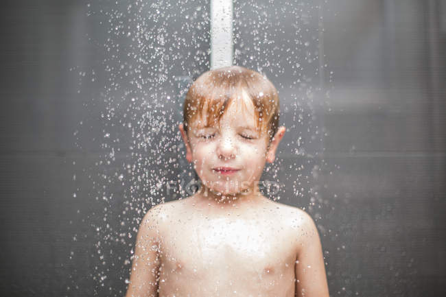 Blond Boy With Eyes Closed Standing Under Water In Shower Indoor 