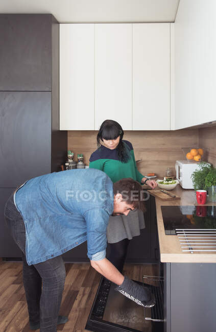 Вид збоку красивий молодий чоловік і красива жінка, дивлячись всередину печі, готуючи їжу в стильній кухні разом — стокове фото