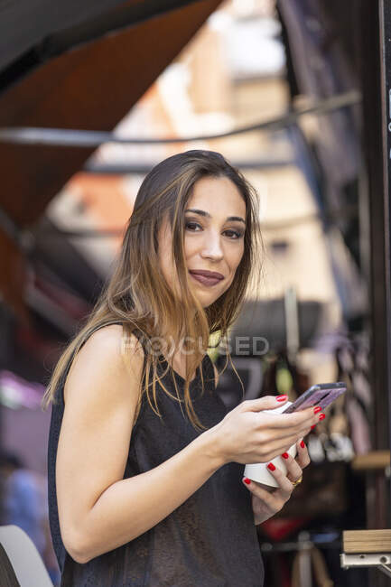 Mulher com bebida e smartphone perto de café ao ar livre — Fotografia de Stock