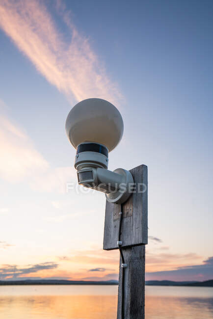Glass lantern on wooden pole on background of still lake and clear sky — Stock Photo
