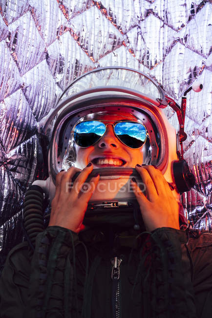 Niña riendo usando casco espacial viejo contra fondo de papel de aluminio - foto de stock