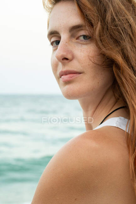 Schöne junge Frau mit Ingwerhaaren schaut weg, während sie auf verschwommenem Hintergrund von Strand und Meer in Tyulenovo, Bulgarien steht — Stockfoto