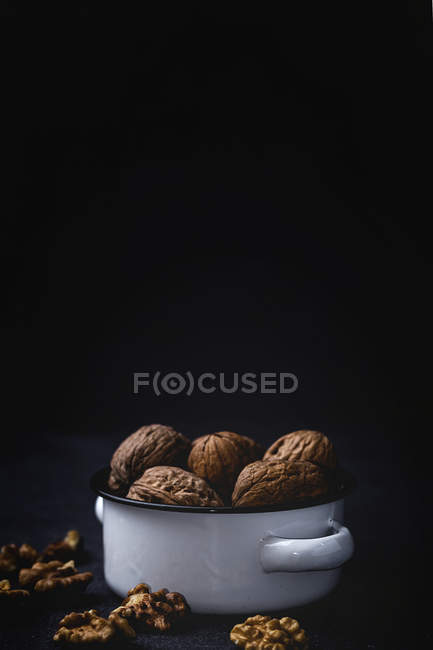 Сушеные оболочки и необработанные грецкие орехи в кастрюле на черном фоне — стоковое фото