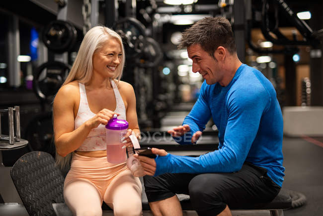 Hombre y mujer en forma alegre sentados en el gimnasio y riendo - foto de stock