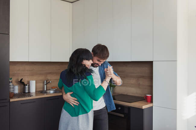 Молодой человек и женщина в повседневных нарядах танцуют вместе, веселясь в стильной кухне дома — стоковое фото