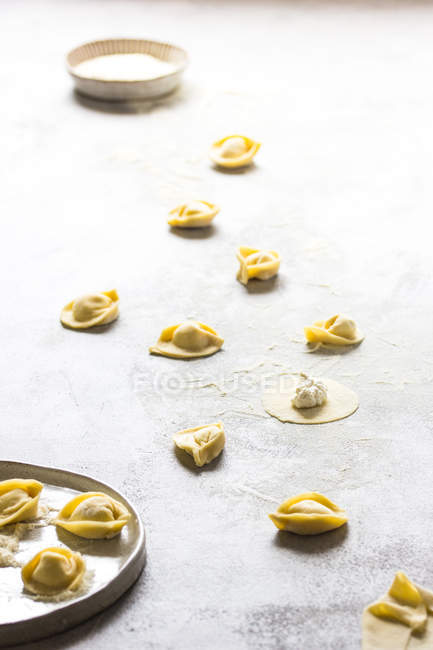 Uncooked tortellini with cottage cheese on floured grey tabletop — Stock Photo