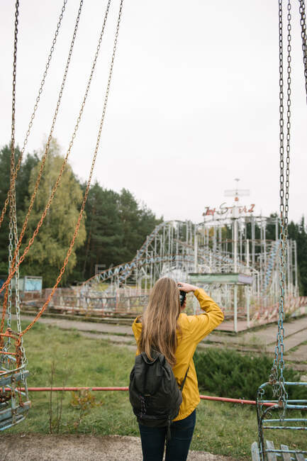 Блондинка с камерой, фотографирующая заброшенный парк развлечений с аттракционами — стоковое фото