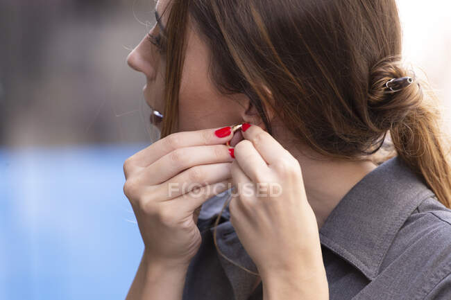 Side view of lovely female putting on cute earring while standing on blurred background of street — Stock Photo