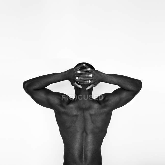 Vista posterior del hombre afroamericano musculoso sin camisa en denim de pie contra la pared blanca - foto de stock