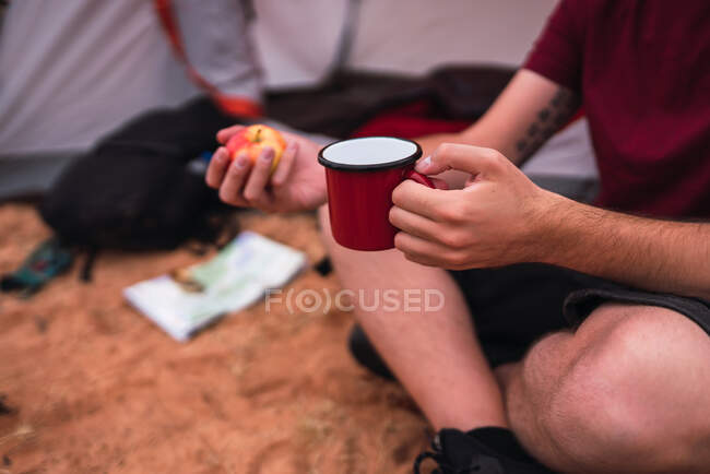 Crop traveler eating apple and with mug near map and compass — Stock Photo