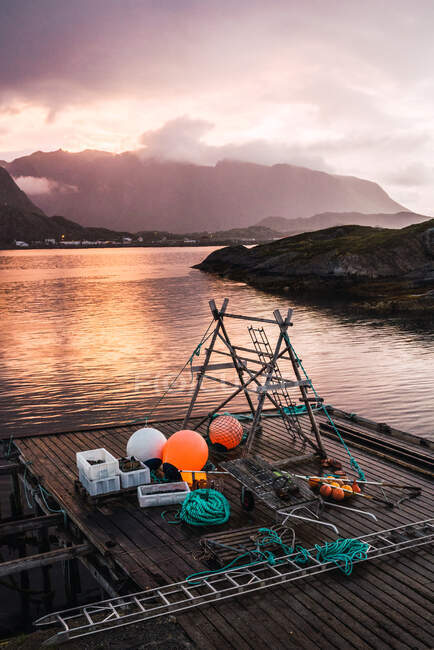 Wooden quay with equipment on clean rippling lake on background of mountains covered with fog and overcast sky — Stock Photo