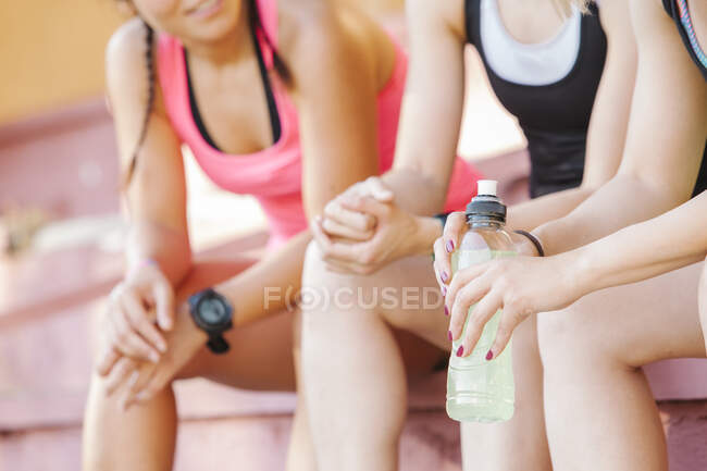 Faceless shot of group of sportive women sitting on stadium tribune with water in bottle — Stock Photo
