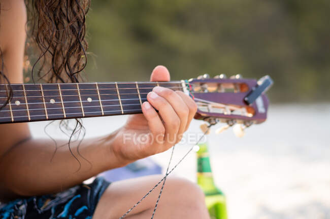 Неупізнаваний хлопець, що грає на гітарі, сидячи на розмитому фоні піщаного пляжу в Тюленово (Болгарія). — стокове фото