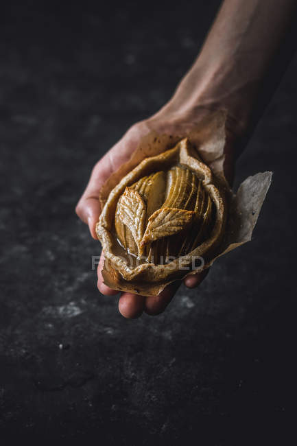 Human hand holding baked apple mini galette on black background — Stock Photo