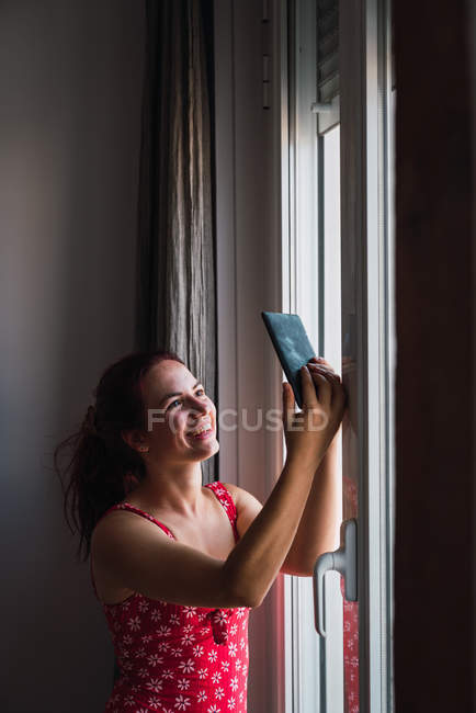 Молодая женщина делает селфи с мобильного телефона рядом с окном дома — стоковое фото