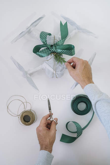 Чоловічі руки обгортають дрон як різдвяний подарунок з ялиновою гілкою та зеленою стрічкою на білому тлі — стокове фото