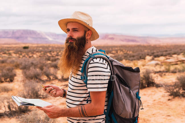 Hombre sosteniendo mapa y brújula retro mientras está de pie sobre un fondo borroso del majestuoso desierto - foto de stock
