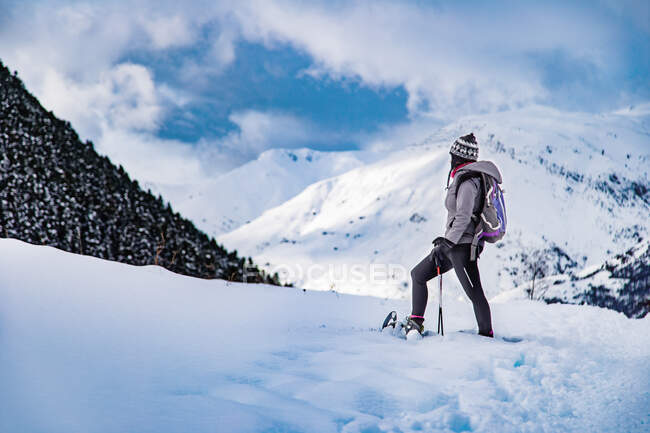 Vista lateral da fêmea em roupas quentes levantando a perna com esqui enquanto está em pé na encosta da montanha nevada — Fotografia de Stock
