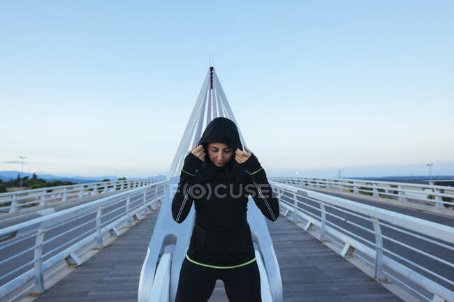 Femme en sportswear noir debout sur la construction moderne du pont regardant confiant — Photo de stock