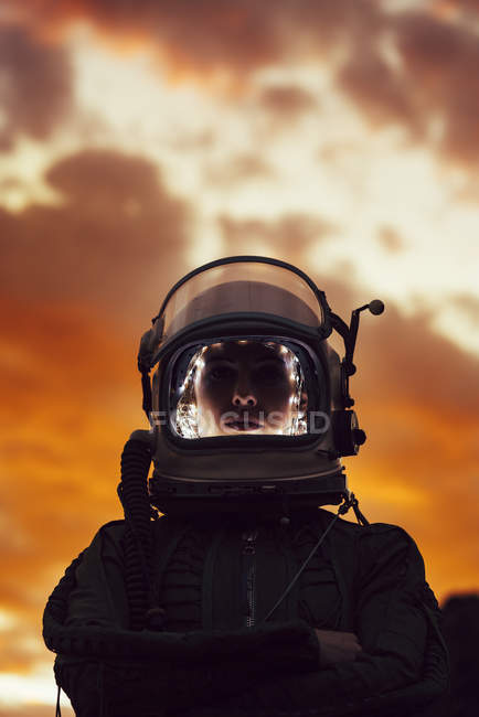 Chica con casco espacial viejo y traje espacial contra el cielo dramático al atardecer - foto de stock