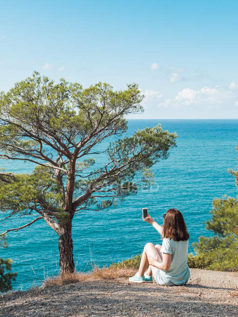 Femme gaie prenant selfie avec téléphone portable sur le bord de mer pittoresque — Photo de stock
