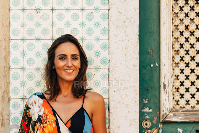 Portrait de jolie femme brune souriante debout contre un vieux mur de bâtiment carrelé à motifs — Photo de stock