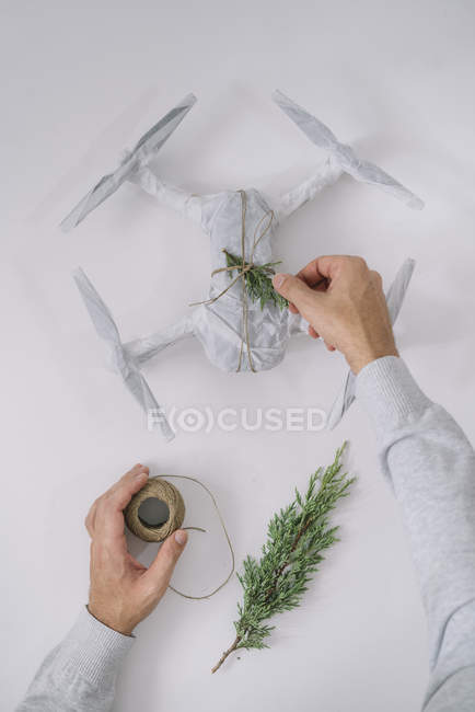 Чоловічі руки прикрашають загорнутий безпілотник як різдвяний подарунок з ялиновою гілкою та шпагатом на білому тлі — стокове фото