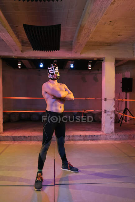 Uomo adulto muscoloso con maschera da lottatore e in piedi con le mani incrociate sul ring — Foto stock