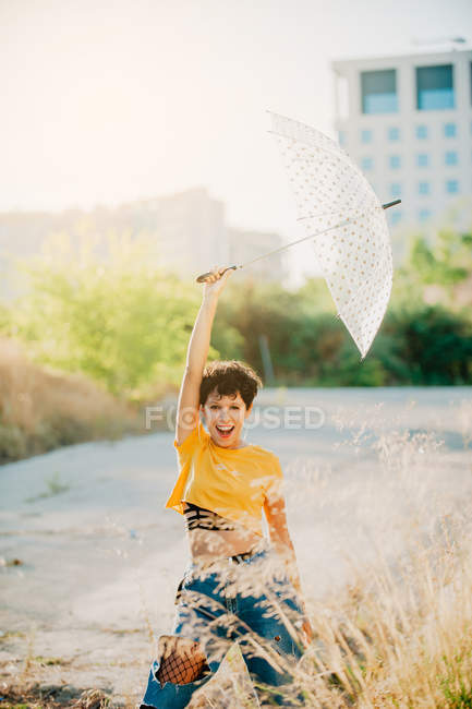 Cheerful young woman holding umbrella outdoors in sunny weather — Stock Photo