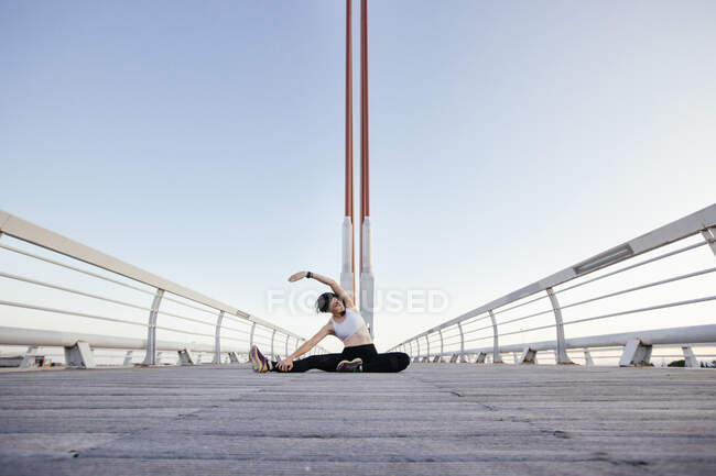 Femme relaxante assise sur le trottoir en bois du pont moderne et s'étirant dans les loisirs regardant loin — Photo de stock