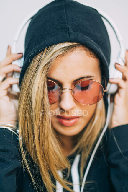 Женщина в черном капюшоне и солнечных очках слушает музыку в наушниках — стоковое фото