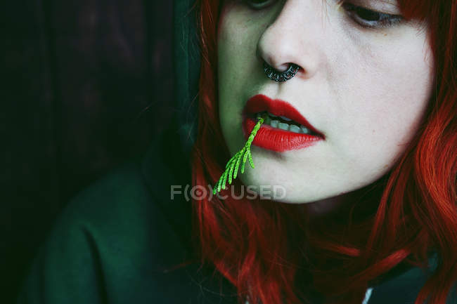 Primo piano di giovane donna dai capelli rossi con piercing e ago di abete in bocca — Foto stock