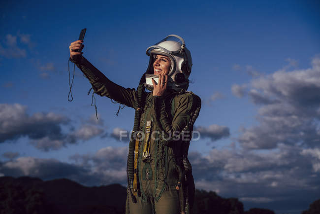 Smiling female astronaut taking selfie mobile phone in evening nature — Stock Photo
