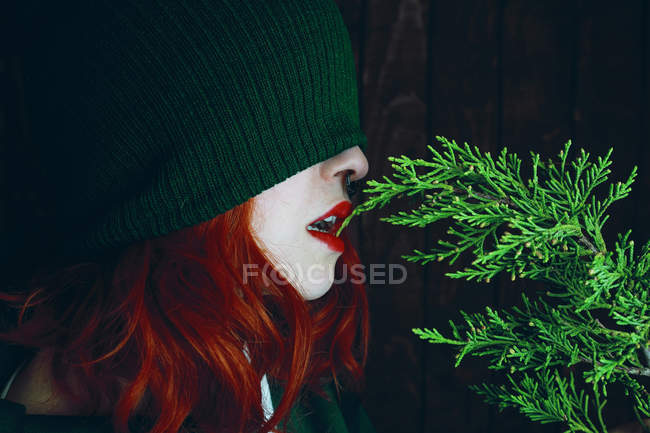 Young red haired woman with red lips and green hat biting fir twig — Stock Photo