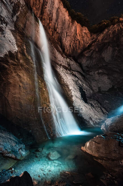 Hermosa cascada clara que fluye desde un alto acantilado rocoso hacia un río puro y poco profundo - foto de stock