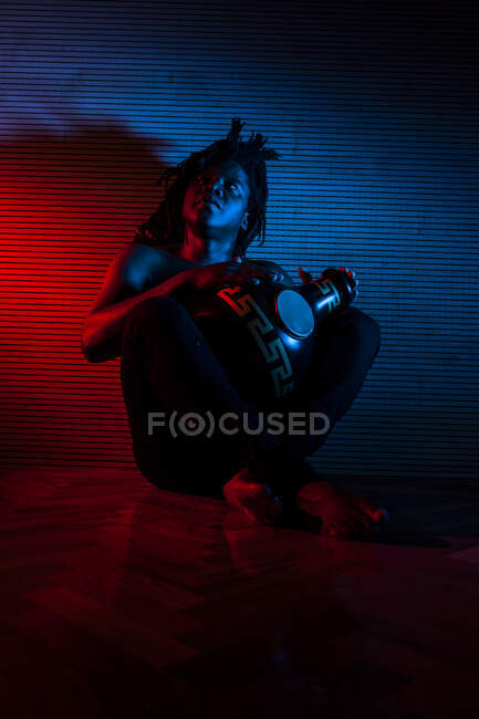 Joven rastafari africano hombre disfruta ensayando y juega udu, iluminación de color rojo y azul - foto de stock