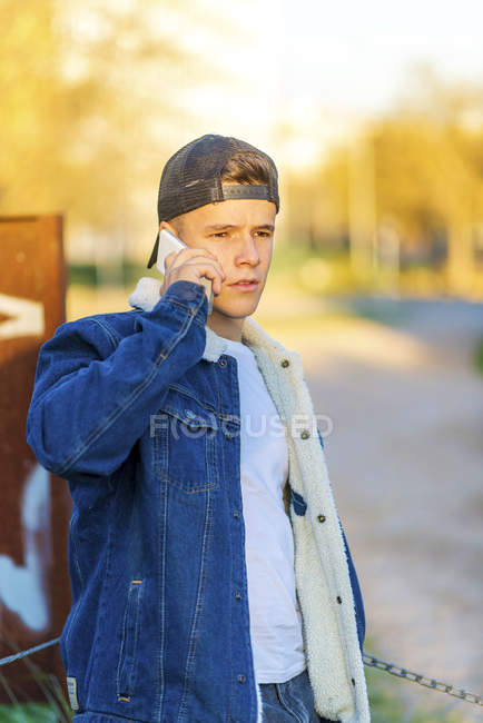 Retrato de um jovem adolescente ao ar livre vestindo trajes casuais e usando um smartphone — Fotografia de Stock