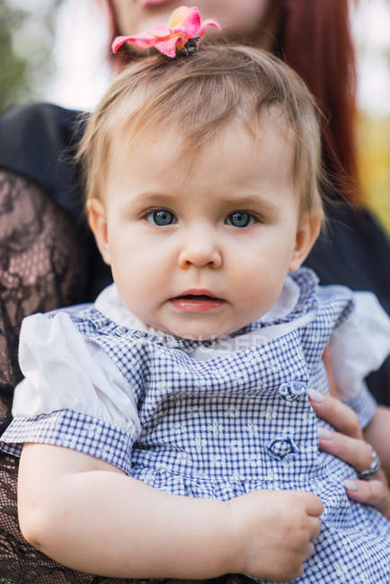 Close-up of cute pensive baby girl sitting on mother lap — Stock Photo