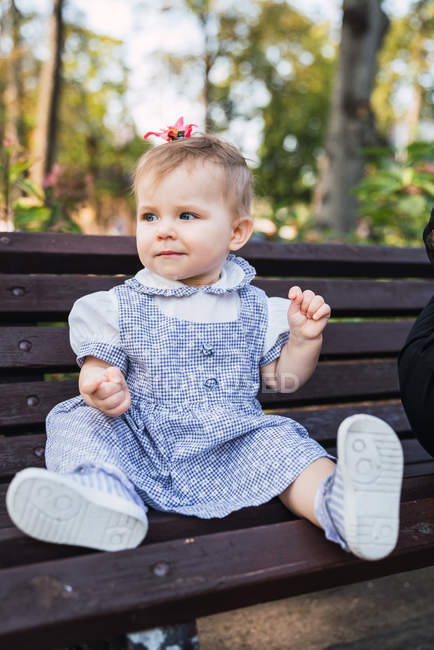 Bebê menina sentada no banco no parque e olhando para longe — Fotografia de Stock
