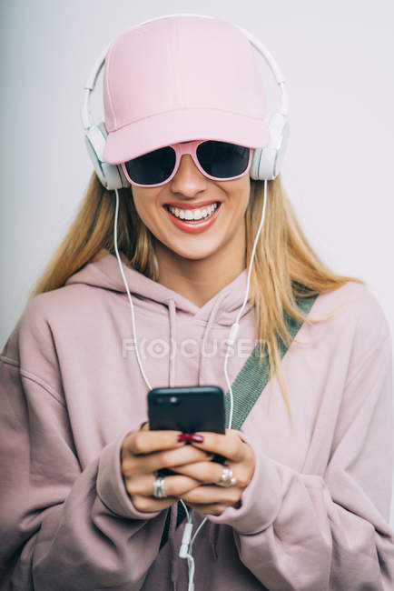 Стильна жінка в рожевому светрі і кепці прослуховування музики з навушниками — стокове фото