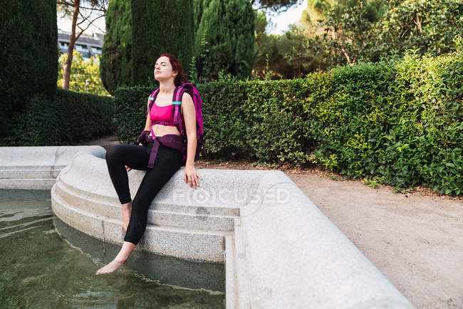 Young sportswoman with backpack sitting on parapet near lake — Stock Photo
