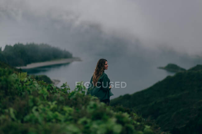 Femme debout sur une haute colline avec un lac en dessous — Photo de stock