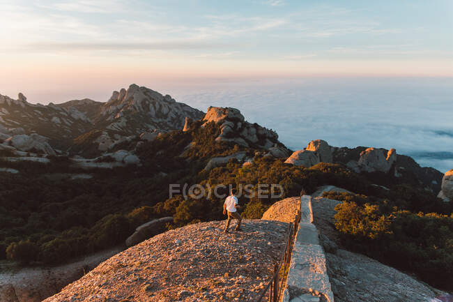Vista posteriore del maschio in abito casual camminare in splendide montagne verso il mare calmo durante l'alba incredibile a Barcellona, Spagna — Foto stock