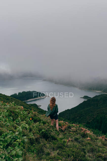 Femme debout sur une haute colline avec un lac en dessous — Photo de stock
