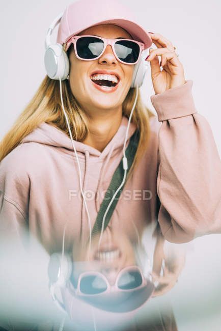 Stylische Frau in rosa Kapuzenpulli und Mütze, die mit Kopfhörern Musik hört — Stockfoto