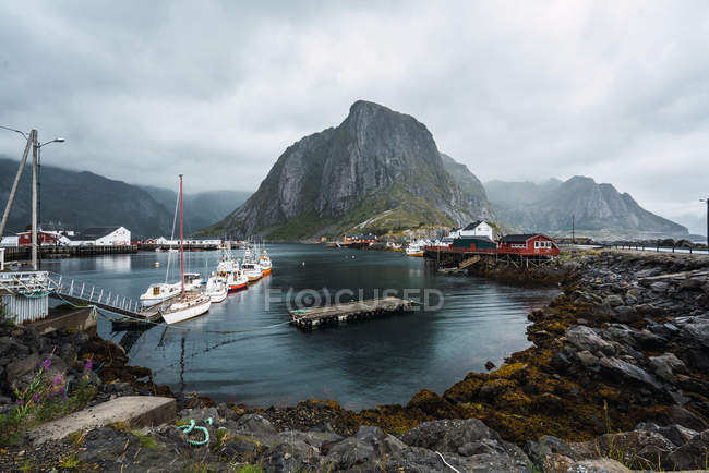 Lake surrounded by rocks with boats sailing on surface on background of mountains covered with fog under overcast sky — Stock Photo