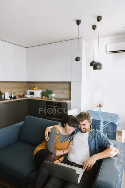 Jovem e mulher abraçando uns aos outros e desfrutando de um bom filme no laptop enquanto se sentam no sofá confortável na acolhedora sala de estar — Fotografia de Stock