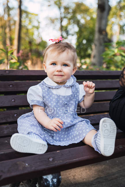 Baby girl sitting on bench in park and looking at camera — Stock Photo